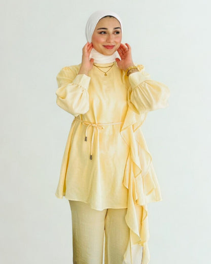 Woman wearing a yellow outfit with a white hijab on a plain background