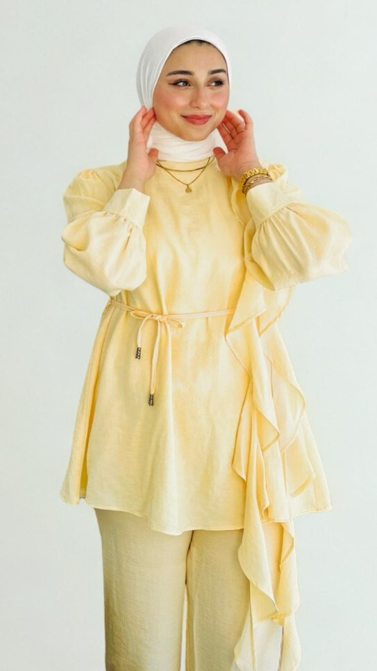 Woman wearing a yellow outfit with a white hijab on a plain background