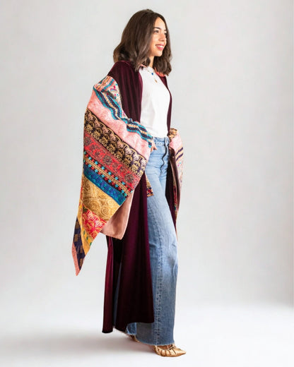 Woman wearing a colorful patterned shawl over a white top and blue jeans on a plain background