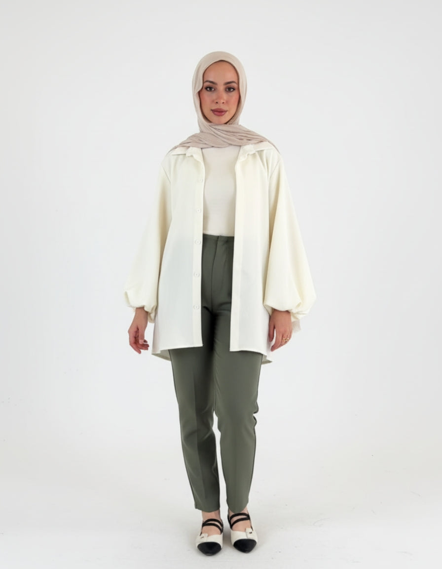 Woman wearing a white blouse, hijab, and green pants on a white background