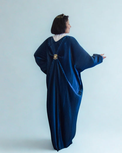 Woman wearing a blue velvet dress with a brooch on a light gray background