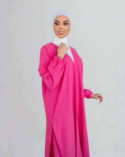 Woman wearing a bright pink dress with a white hijab on a light gray background