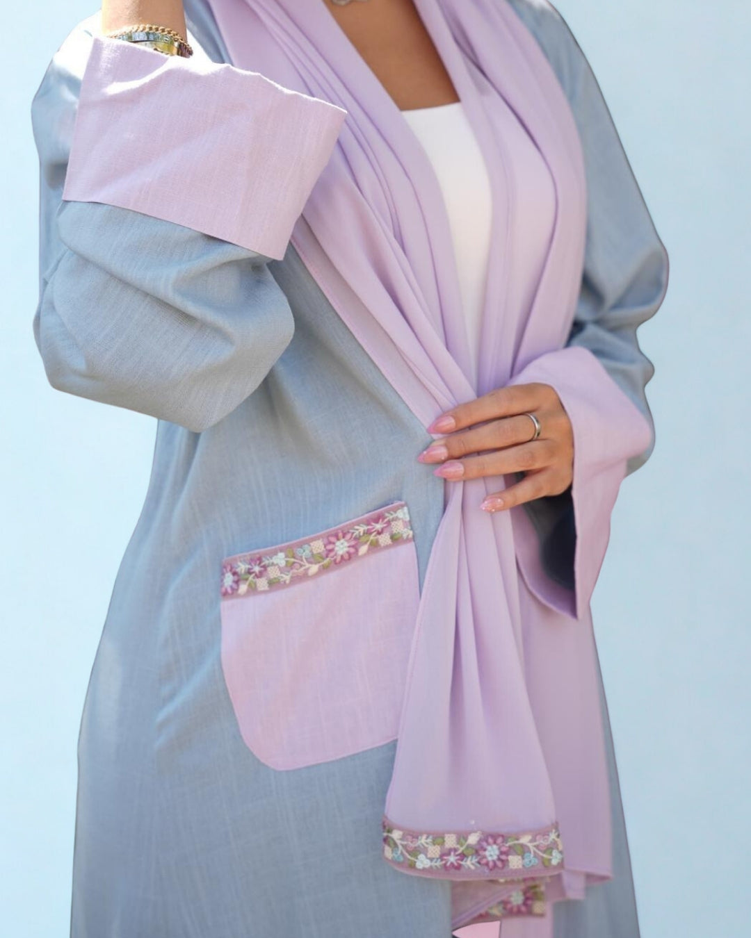 Person wearing a light blue dress with a pink hijab against a clear sky