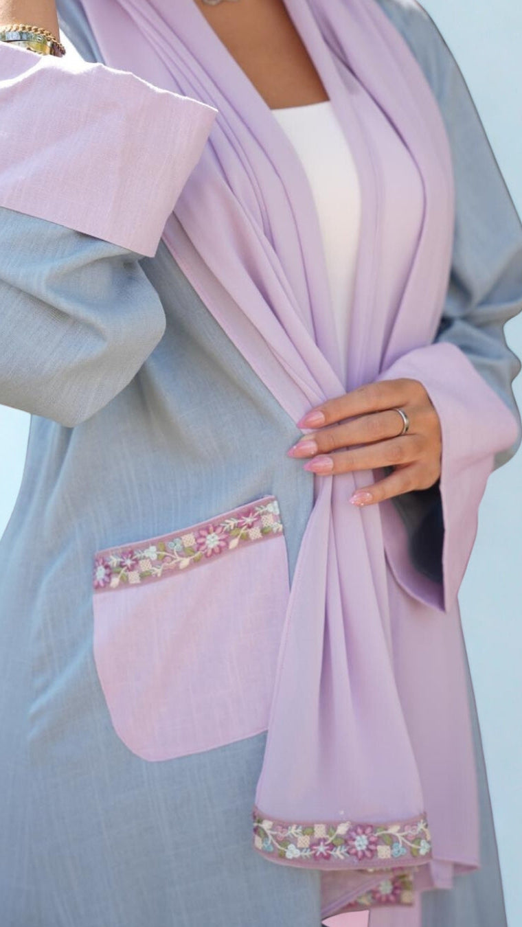 Person wearing a light blue dress with a pink hijab against a clear sky