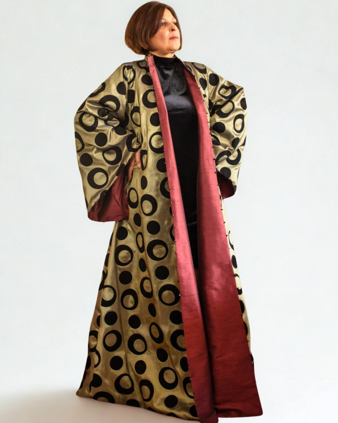 Woman wearing a long, patterned coat with a red interior on a white background
