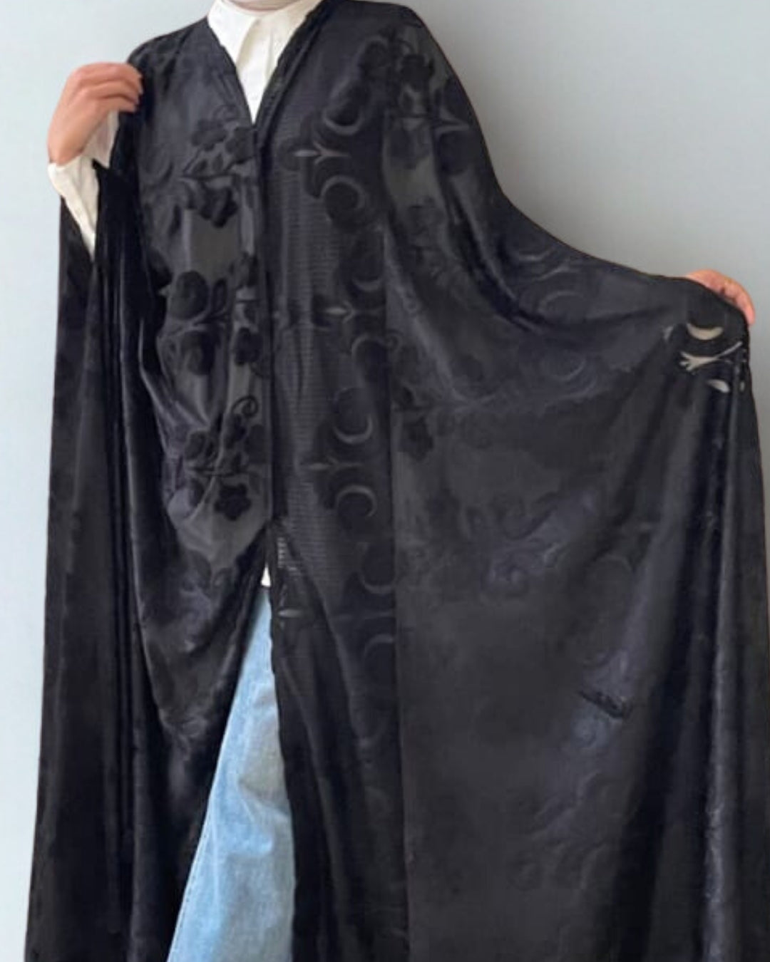 Person wearing a black embroidered robe against a white background