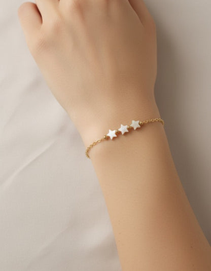 Gold bracelet with star charms on a wrist against a neutral background