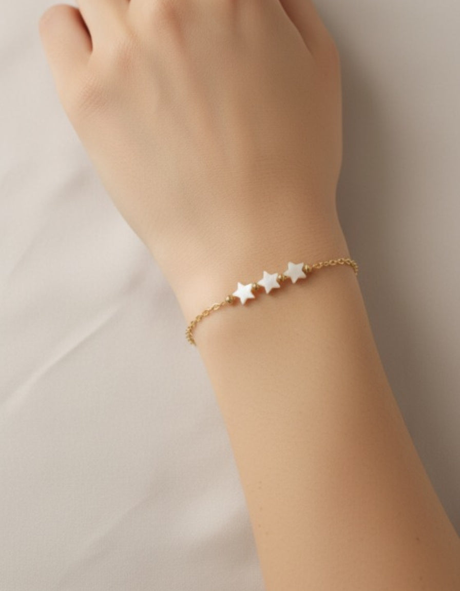 Gold bracelet with star charms on a wrist against a neutral background