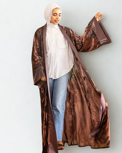 Person wearing a long brown coat over a white top and blue jeans on a light gray background