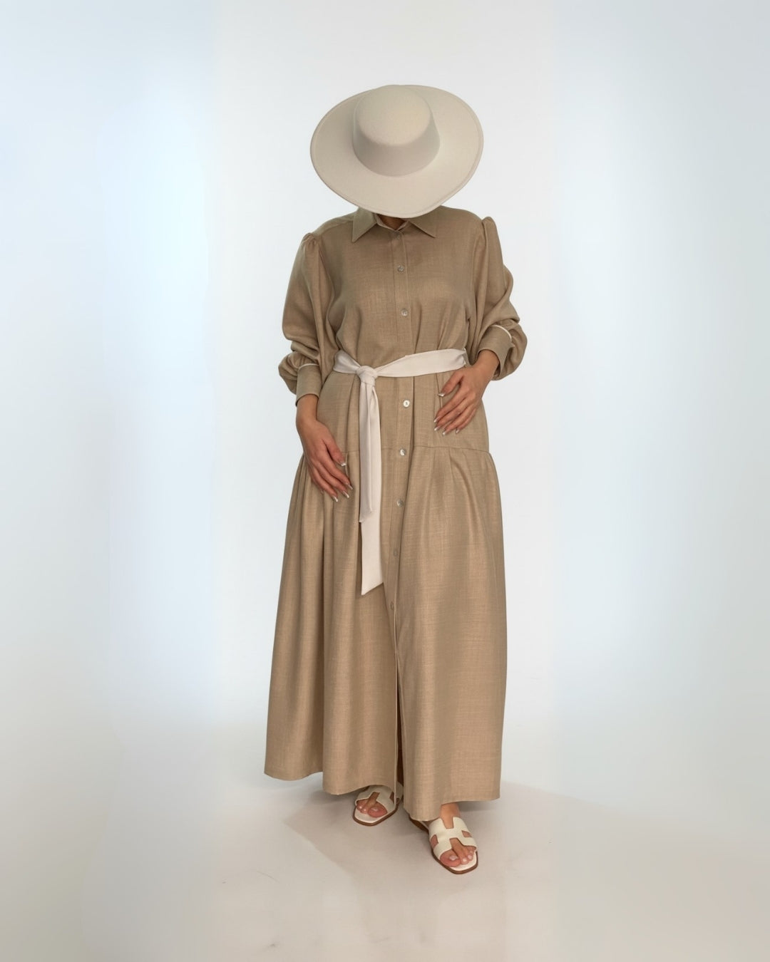 Person wearing a beige dress and hat against a white background