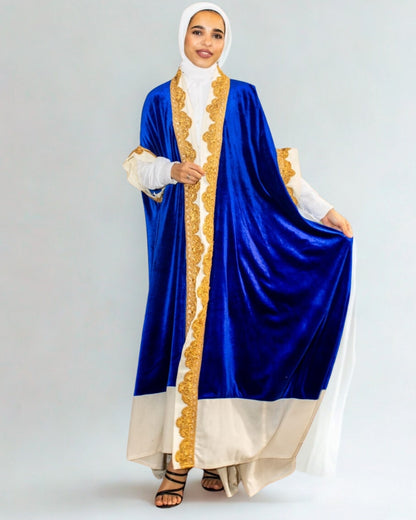 Woman wearing a blue and gold abaya with a white hijab on a gray background