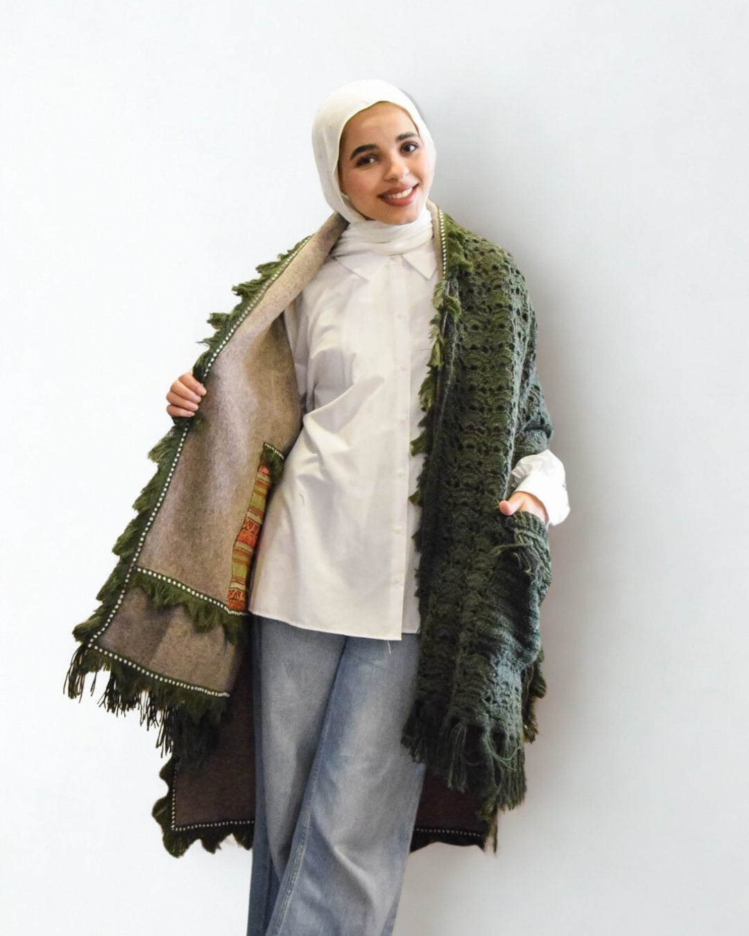 Woman wearing a green textured scarf over a white top and light blue pants on a white background