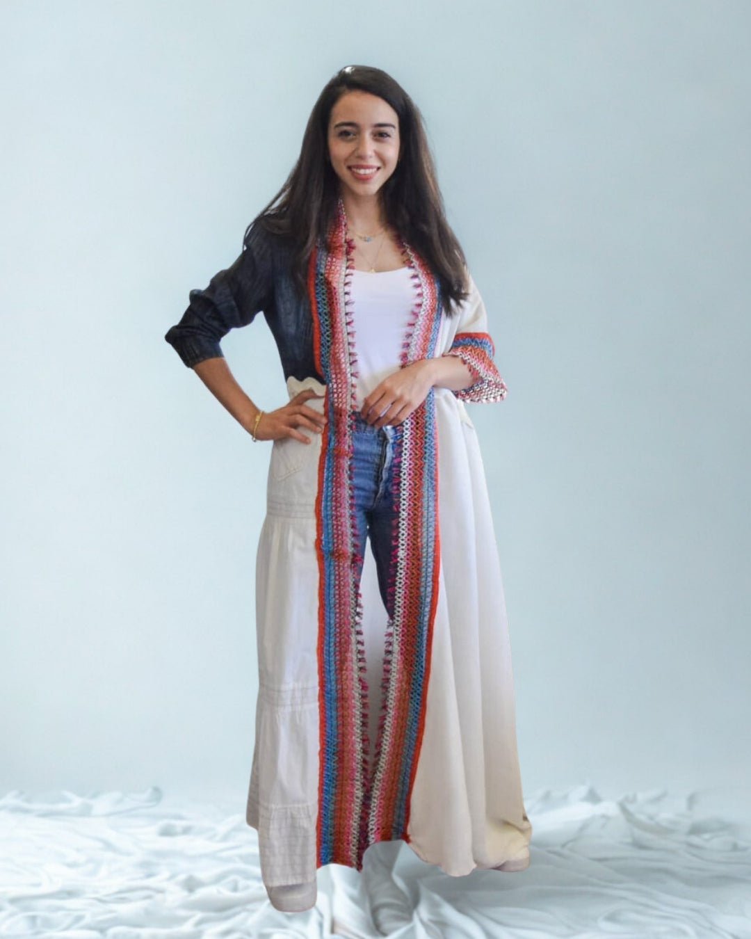 Woman wearing a colorful striped cardigan over a white top and beige pants on a light gray background