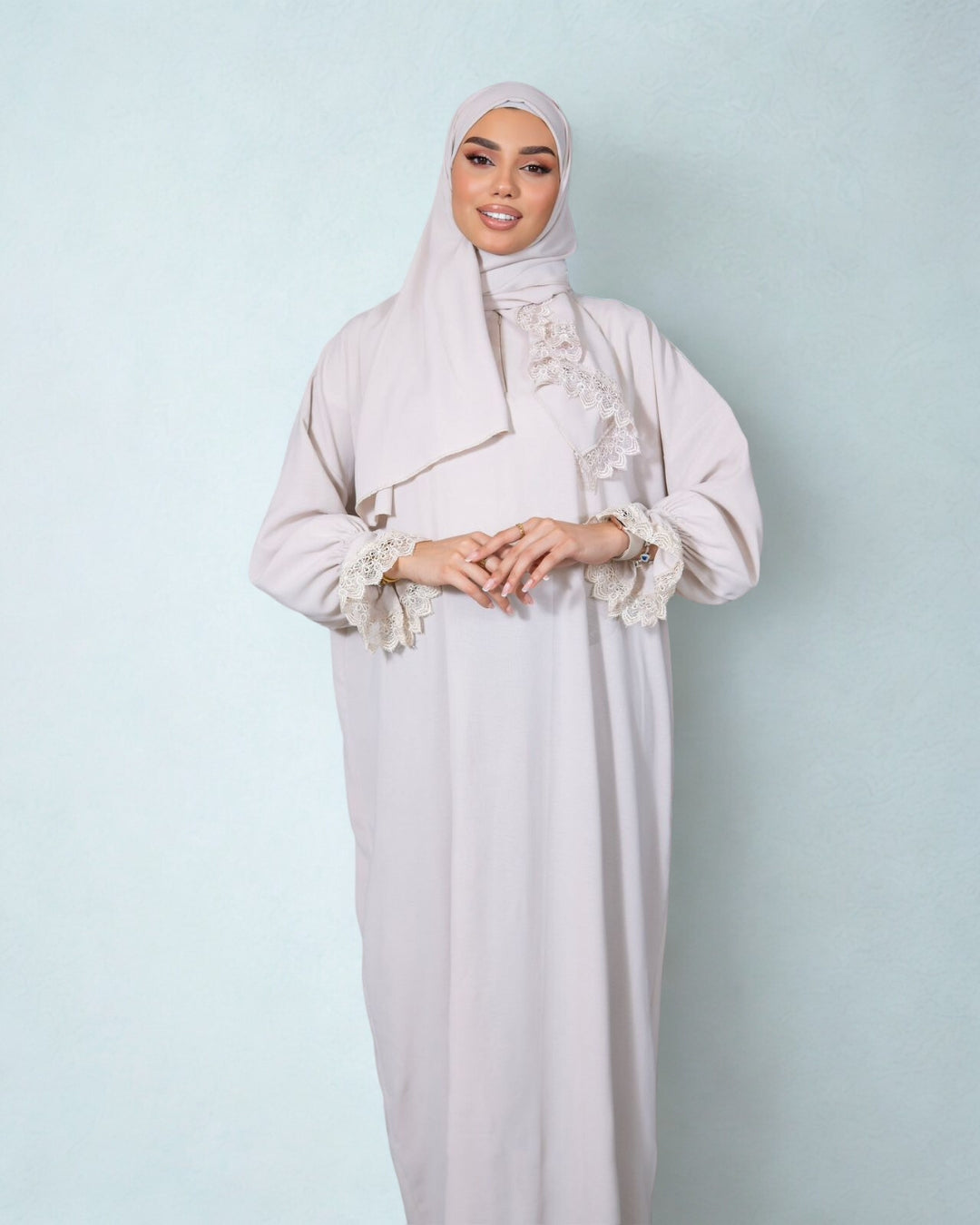 Woman wearing a light gray hijab and dress against a light blue background