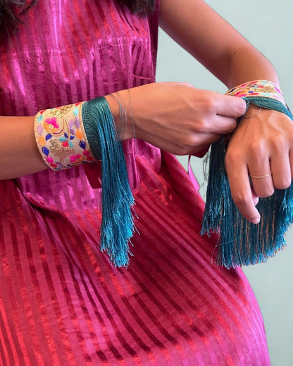 Person wearing a pink traditional outfit with colorful bangles and turquoise tassels.