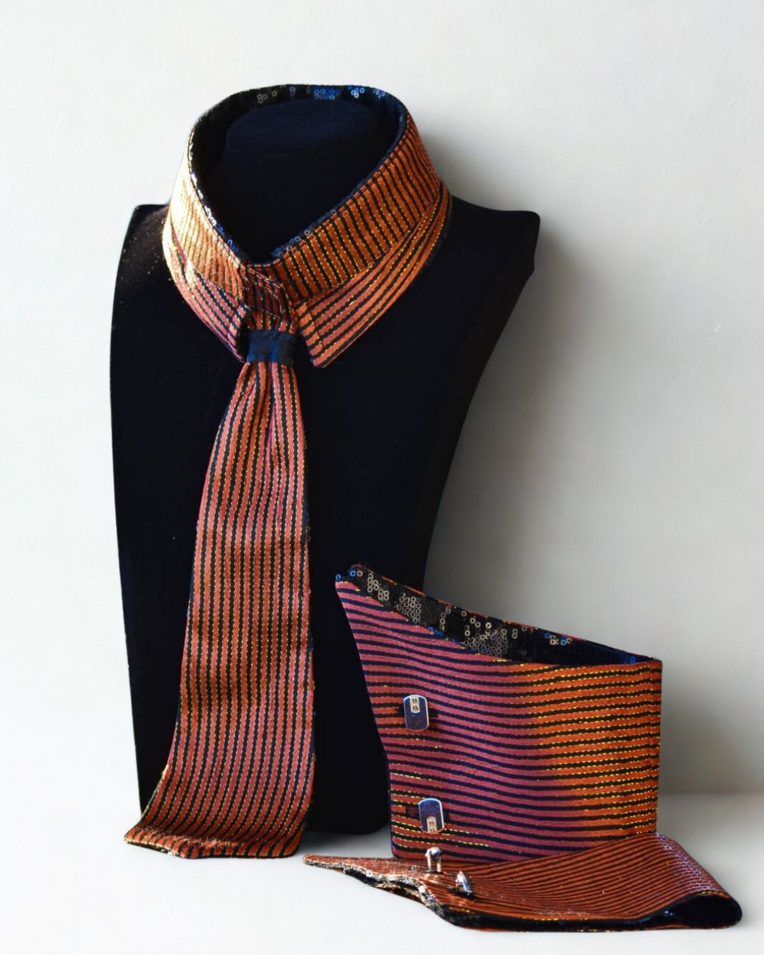 Patterned tie and cufflinks set on a black mannequin against a white background