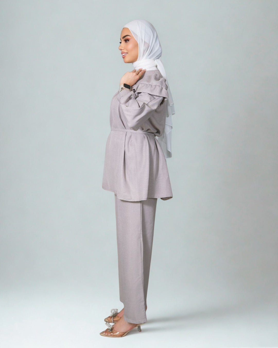 Woman wearing a light gray outfit with a matching hijab on a white background