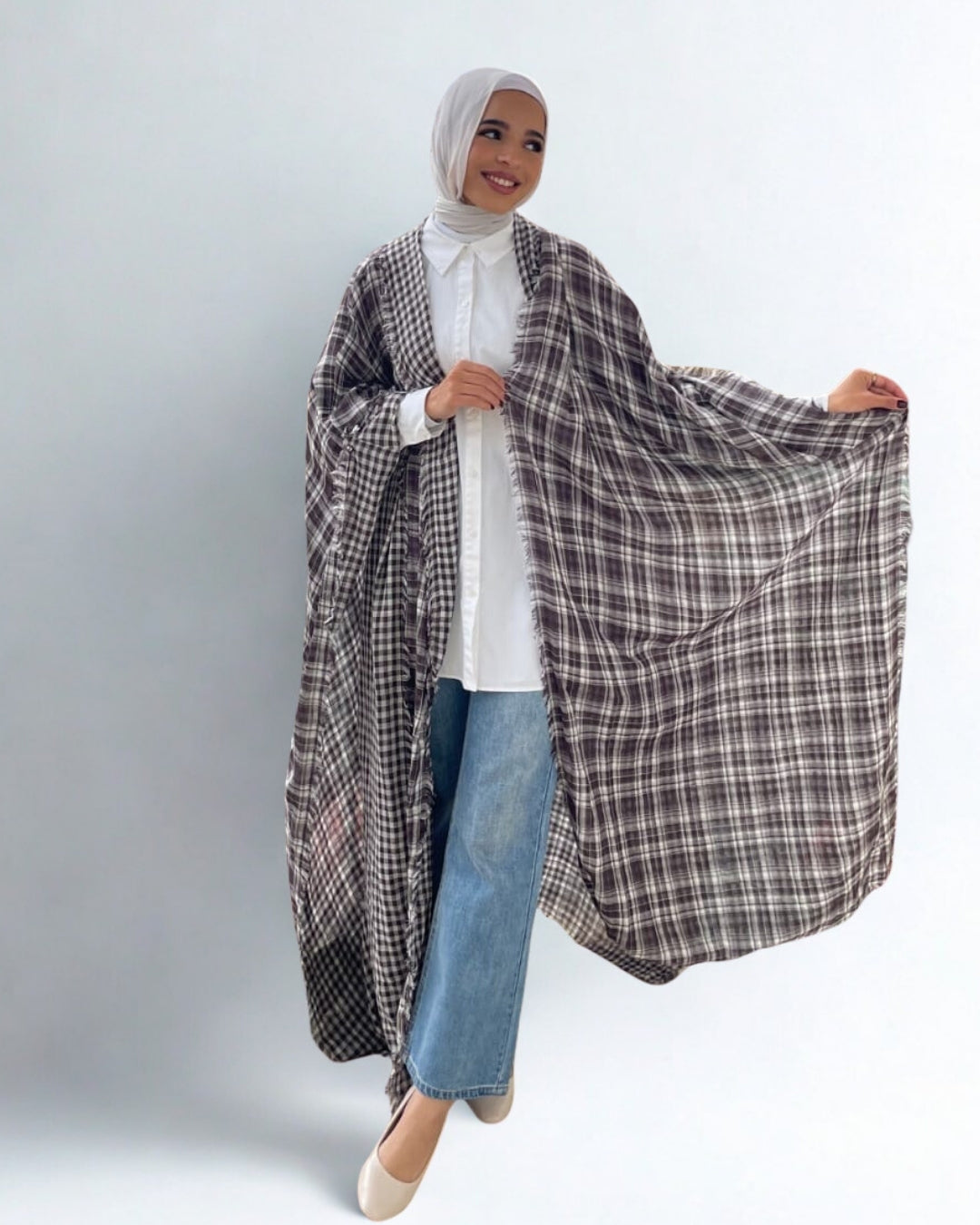Person wearing a plaid shawl over a white shirt and jeans on a plain background
