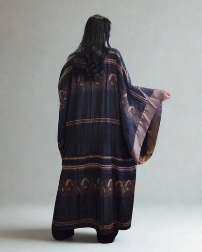 Person wearing a dark blue poncho with brown patterns on a plain background