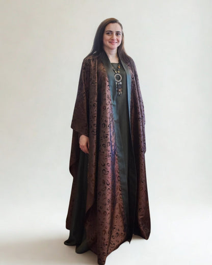 Woman wearing a long, dark brown coat with intricate patterns on a white background