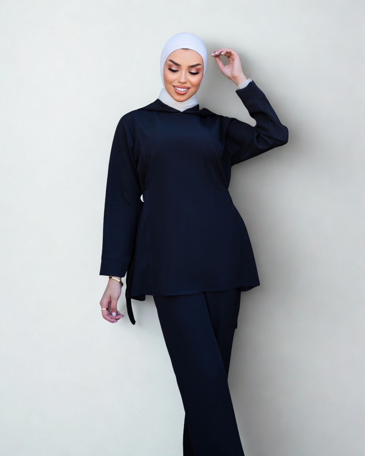 Woman wearing a navy blue outfit with a white hijab against a light gray background