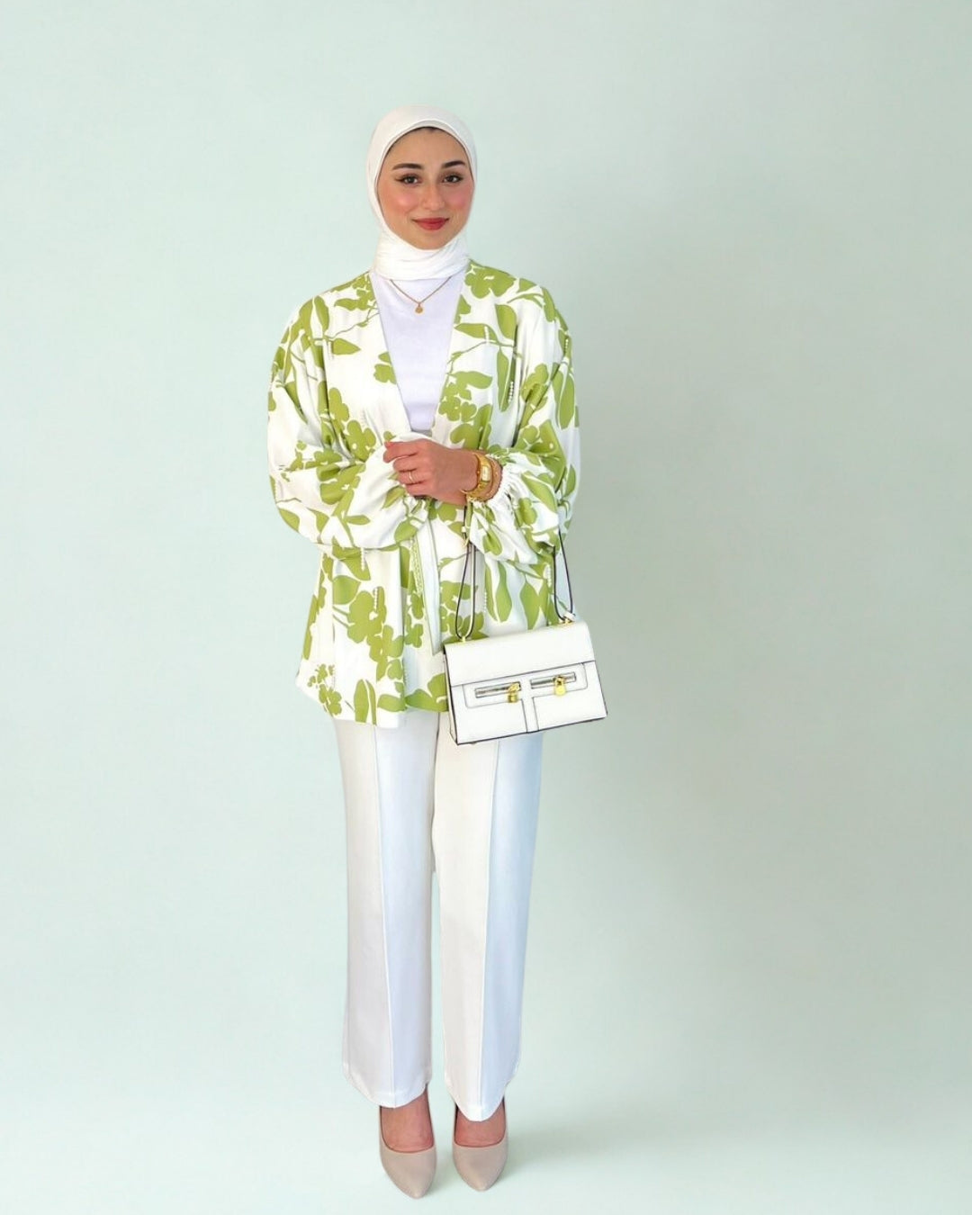 Woman wearing a green and white patterned blazer with white pants on a plain background