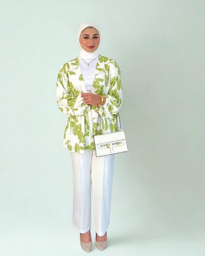 Woman wearing a green and white patterned blazer with white pants on a plain background