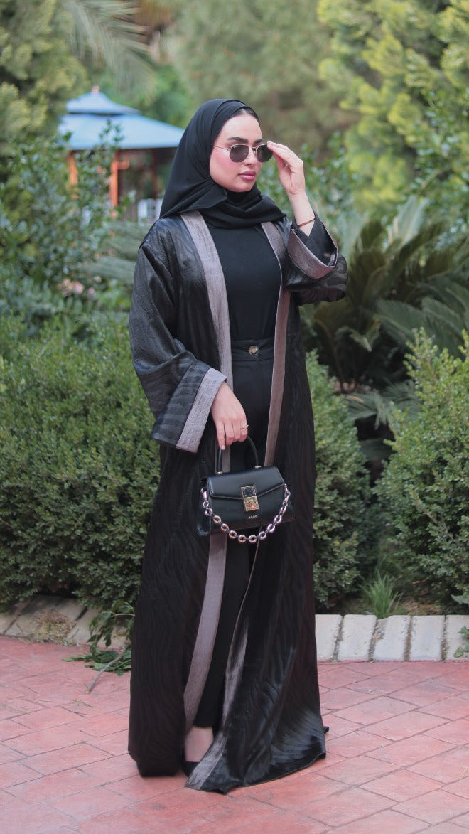 Woman in a black and gray dress standing outdoors with greenery in the background