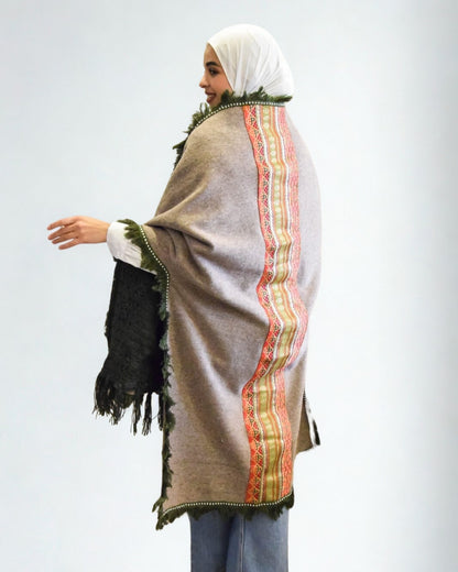 Person wearing a patterned shawl with a colorful border on a plain background