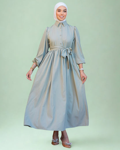 Woman wearing a long light gray dress with a belt on a light green background