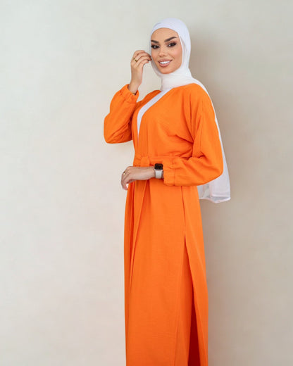 Woman wearing an orange dress with a white hijab on a plain background