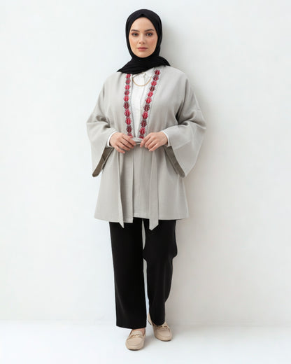 Woman wearing a light gray top with red embroidery and black hijab on a white background