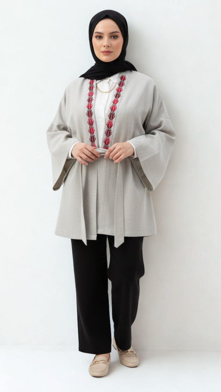 Woman wearing a light gray top with red embroidery and black hijab on a white background
