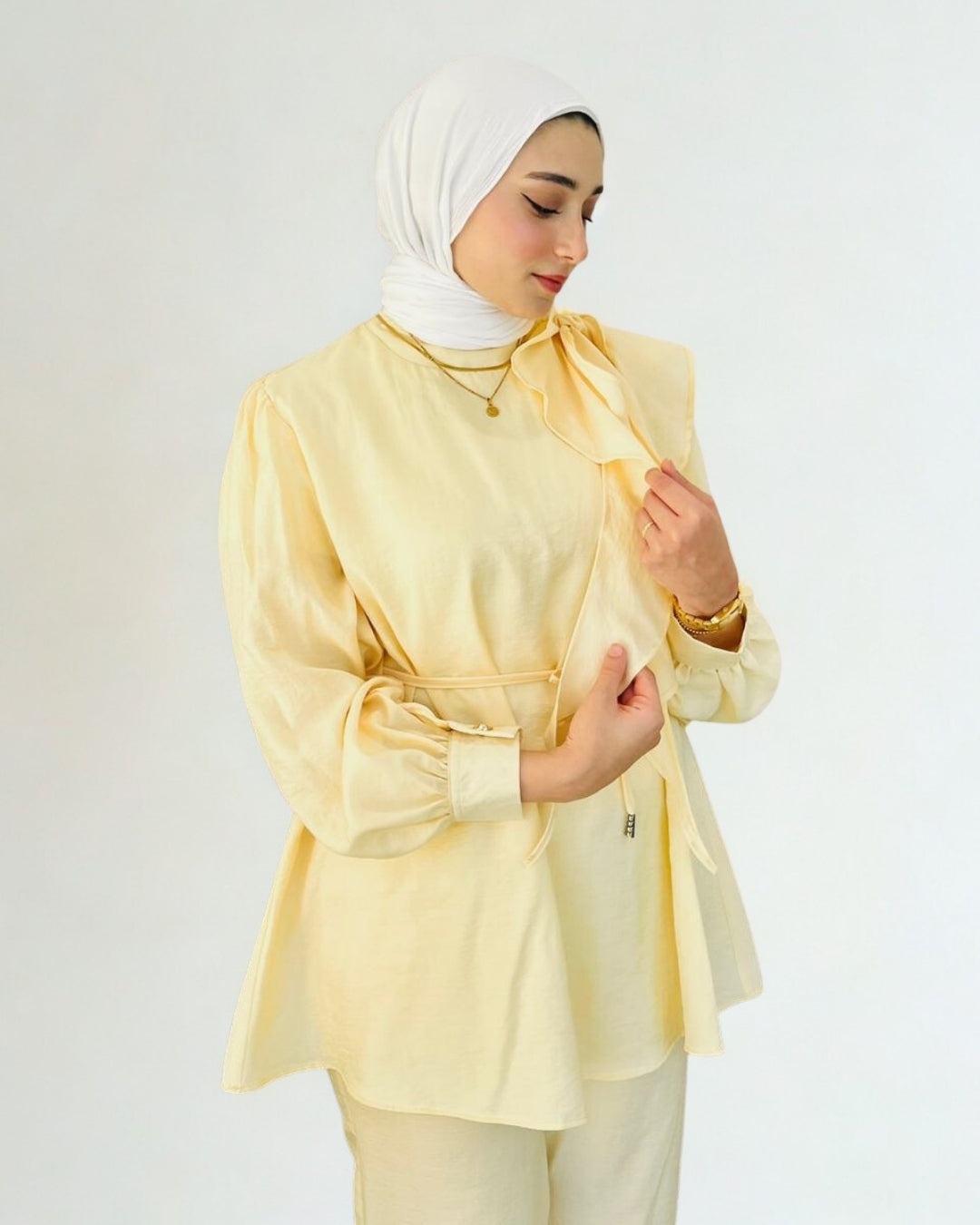 Woman wearing a light yellow outfit with a matching hijab against a white background