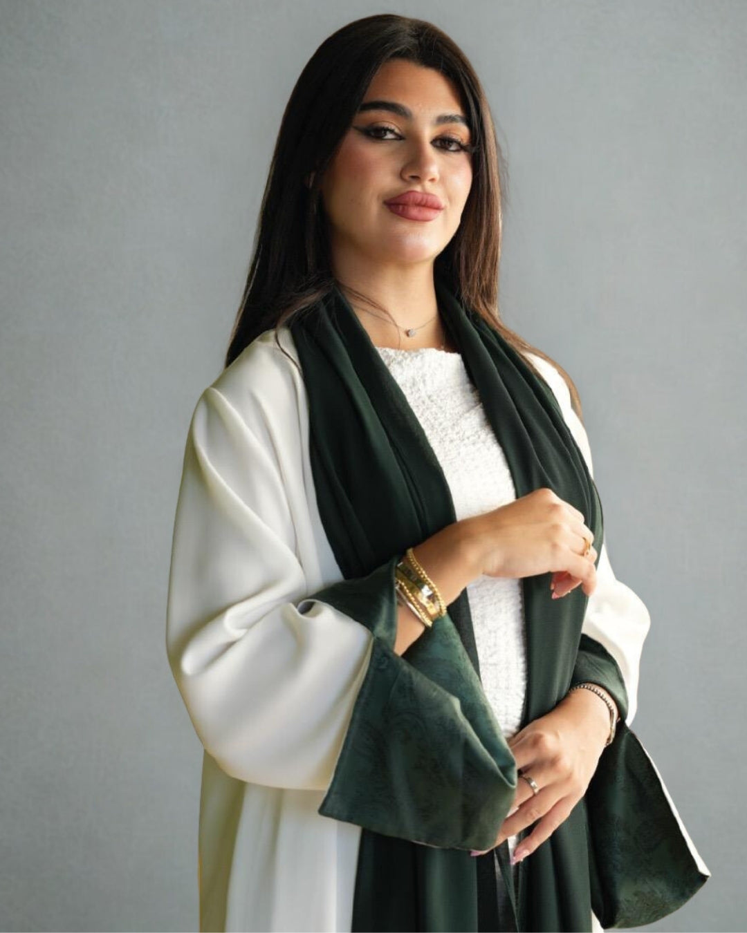Woman wearing a white outfit with a dark green scarf against a gray background