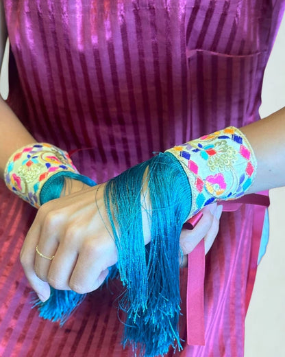 Person wearing colorful bangles with blue thread, against a pink background