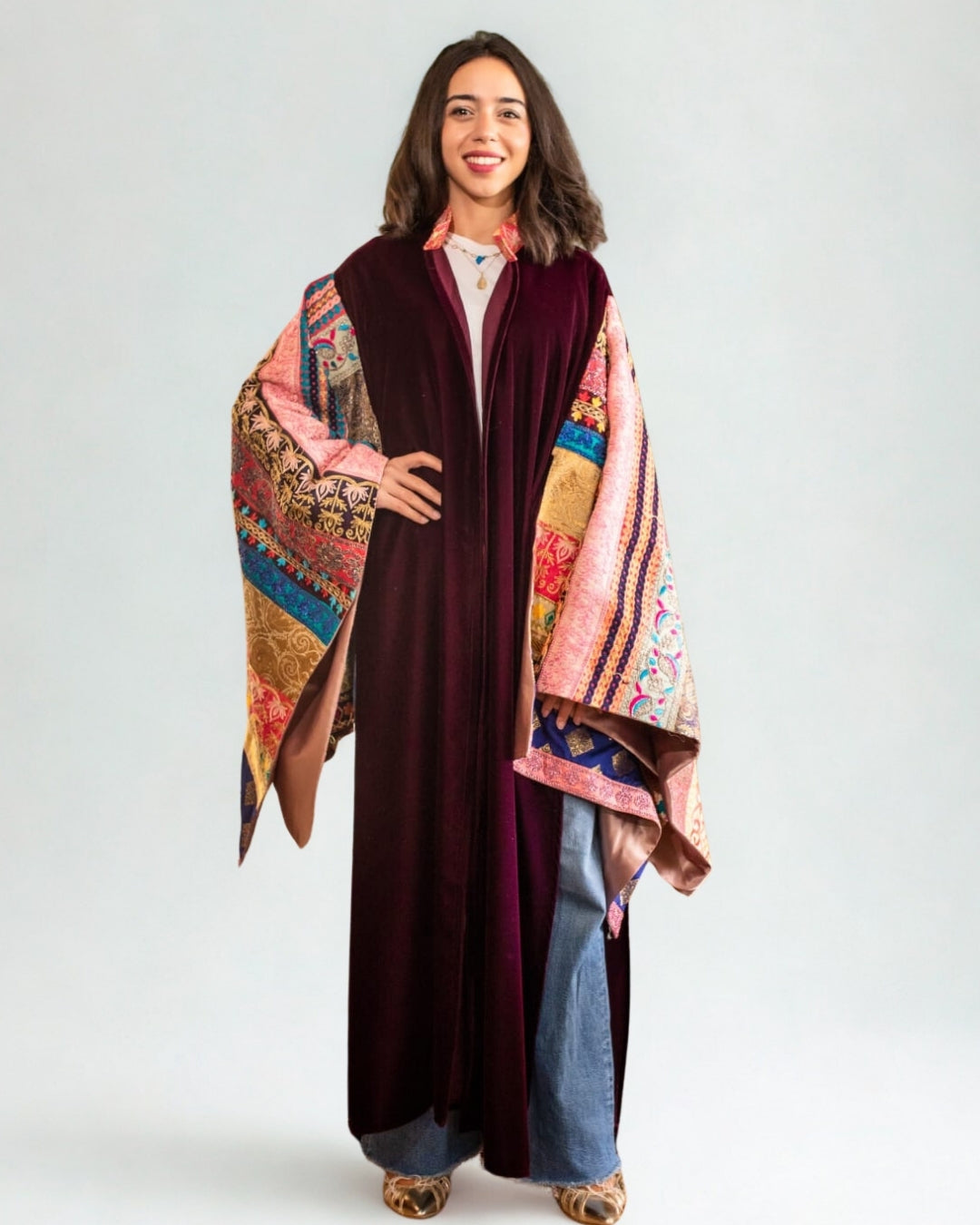 Woman wearing a long, dark-colored dress with a colorful, patterned shawl over her shoulders against a white background.