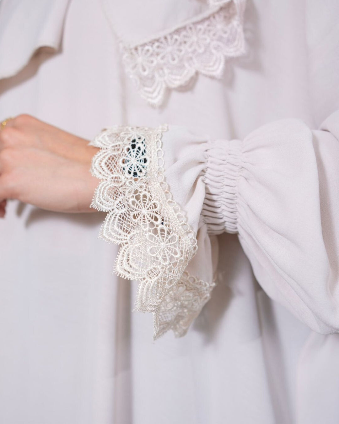 Close-up of a white garment with lace detailing on cuffs and neckline.