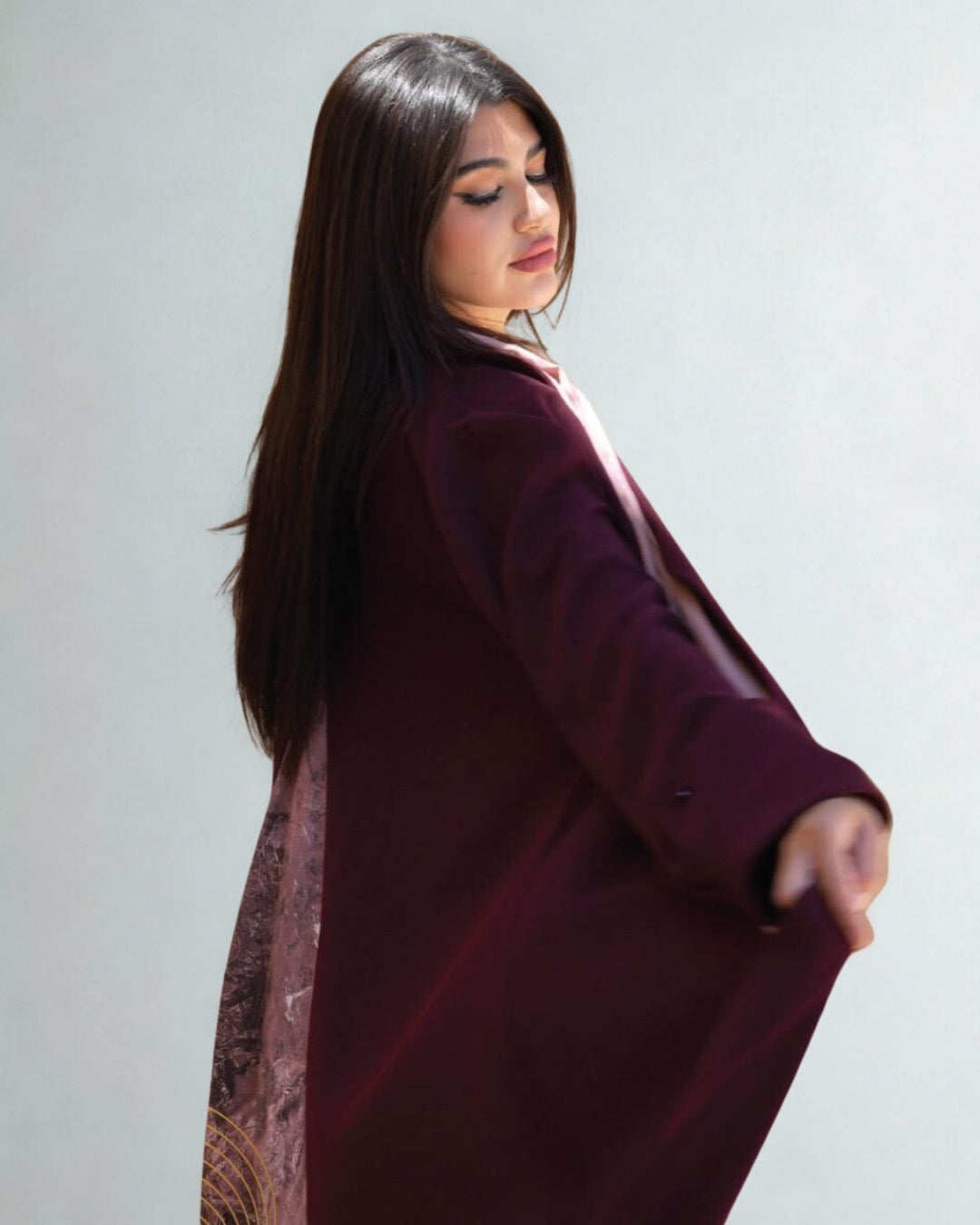Woman wearing a burgundy coat with a patterned scarf against a plain background