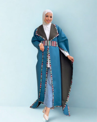 Woman wearing a blue and black abaya with colorful trim on a light blue background