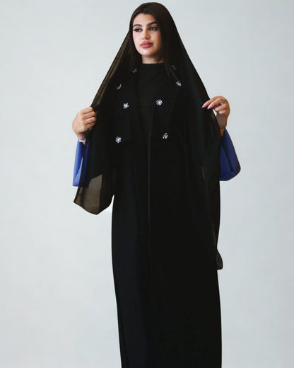 Woman wearing a black abaya with blue accents on a white background