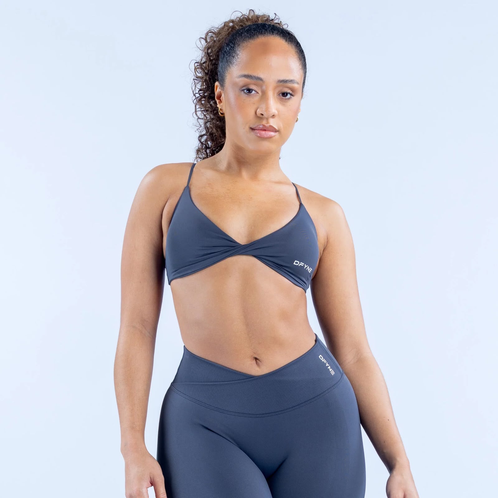 Woman wearing a gray sports bra and leggings with a light blue background