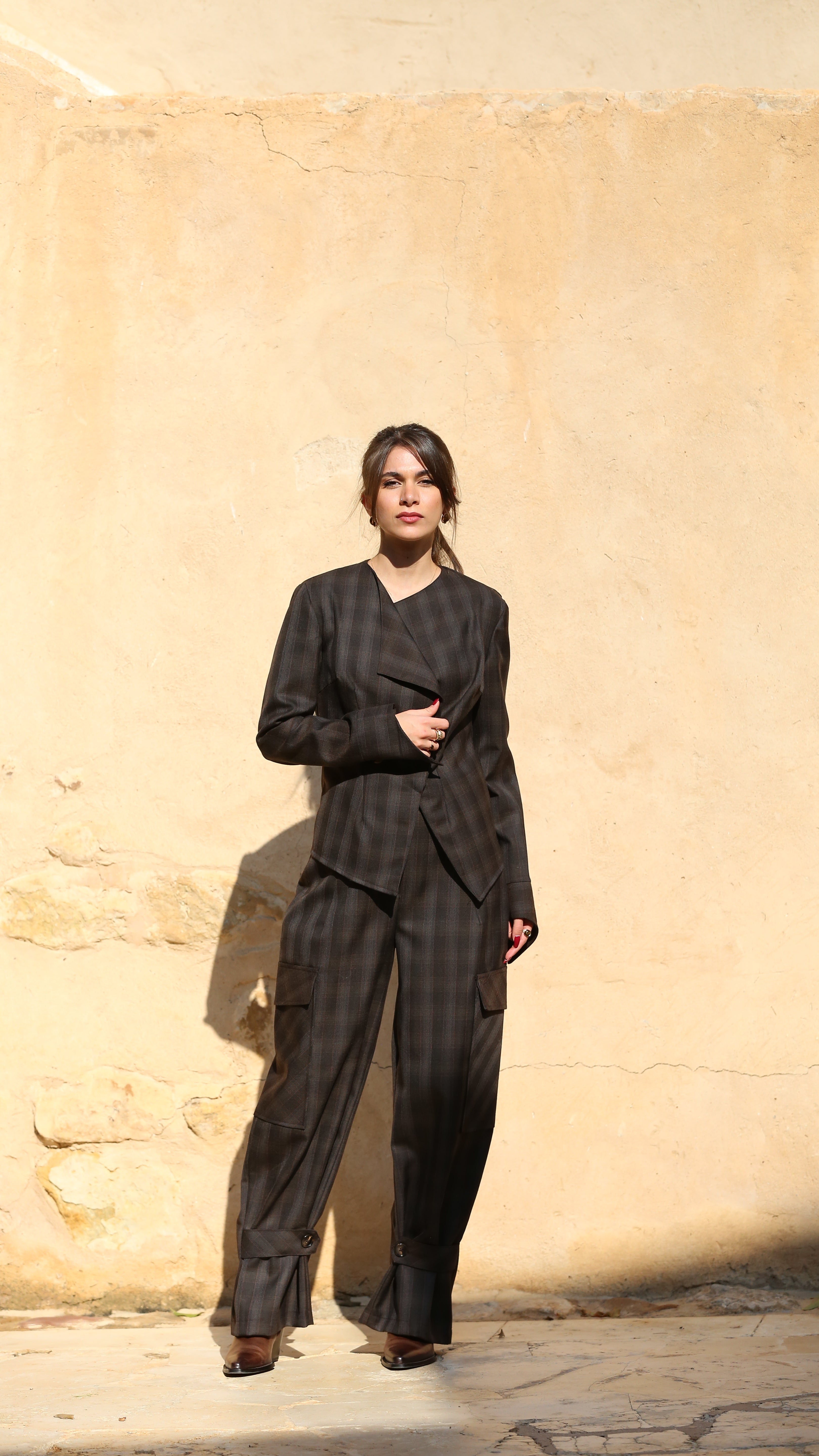 Woman in a black outfit standing against a beige stone wall.