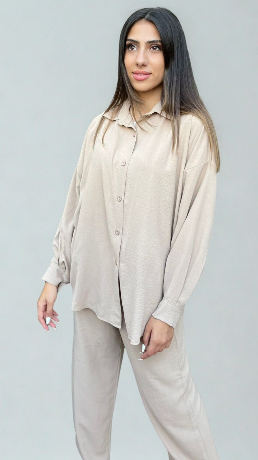 Woman wearing a beige shirt and pants set against a plain background