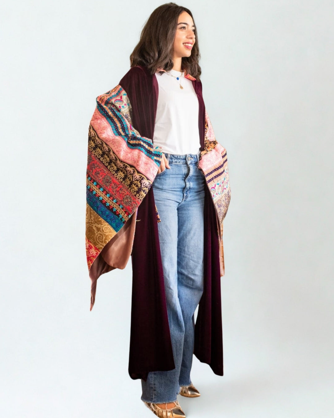 Woman wearing a colorful patterned shawl over a plain white shirt and blue jeans on a white background