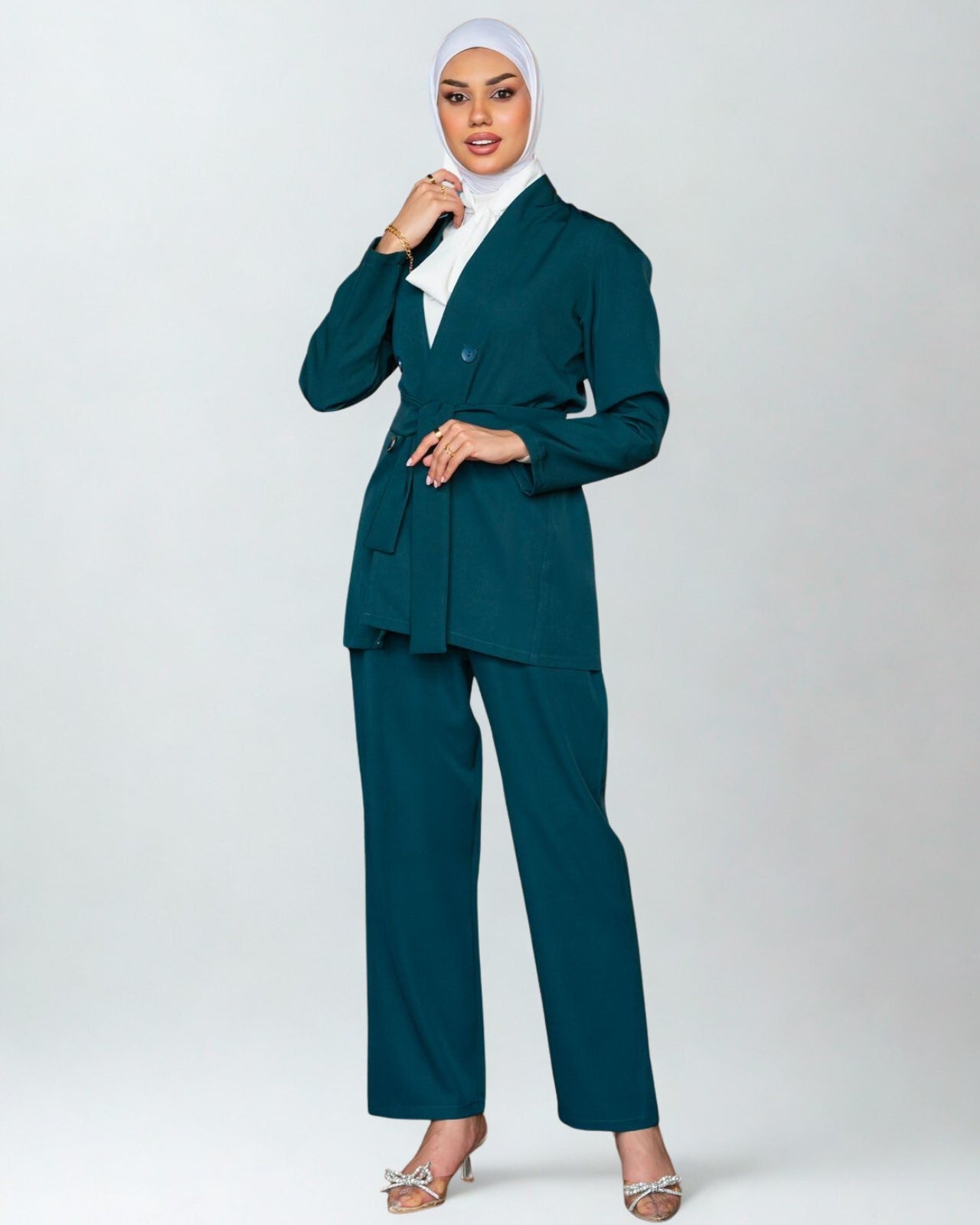 Woman wearing a teal suit with a white hijab on a white background