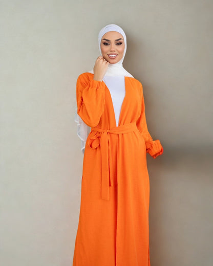Woman wearing an orange dress with a white hijab against a beige background
