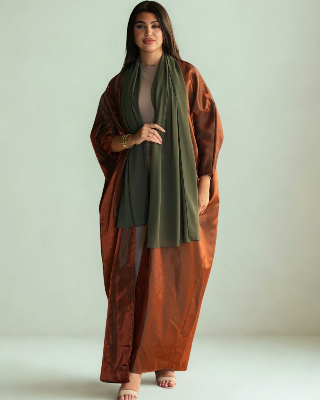 Woman wearing a long rust-colored coat over a green dress on a plain background