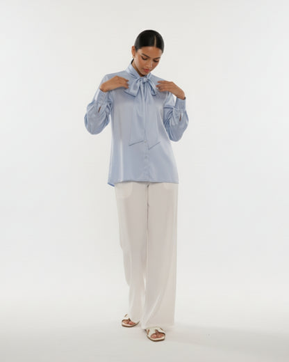 Woman wearing a light blue blouse with a bow and white pants on a white background