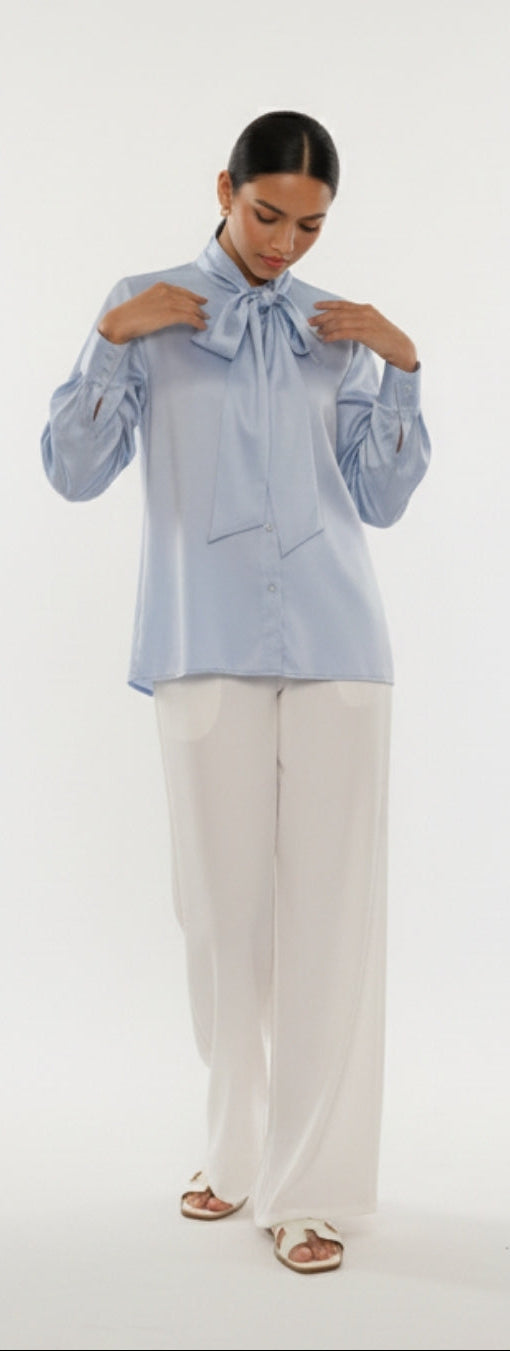 Woman wearing a light blue blouse with a bow and white pants on a white background